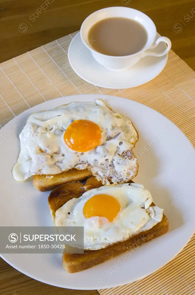 Food And Drink, Cooked, Eggs, A Breakfast Table Setting Of Two Fried Eggs On Toast On A Plate Beside A Cup Of Tea In A Saucer.