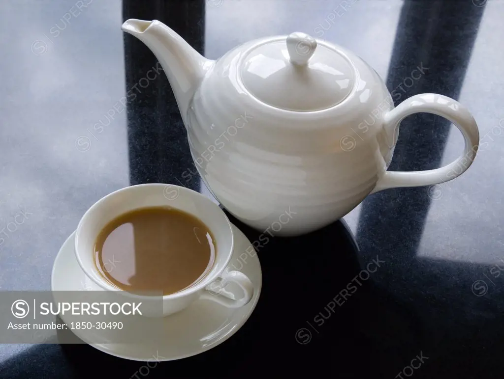 Drinks, Hot, Tea, Cup Of Tea In A Cup And Saucer Beside A Teapot On A Black Granite Kitchen Worktop With Clouds And Sky Reflected.