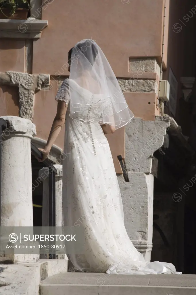 Italy Veneto Venice, Bride in white wedding dress and veil  standing on canal bridge