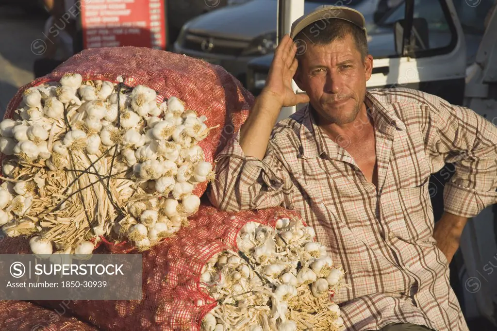 Turkey Aydin Province KUSAdasi, Stallholder at weekly market leaning on sacks of garlic