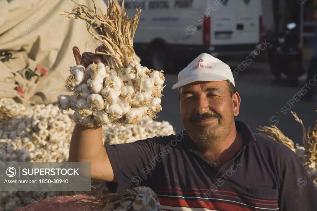 Turkey Aydin Province KUSAdasi, Stallholder at weekly market holding up bunch of garlic bulbs