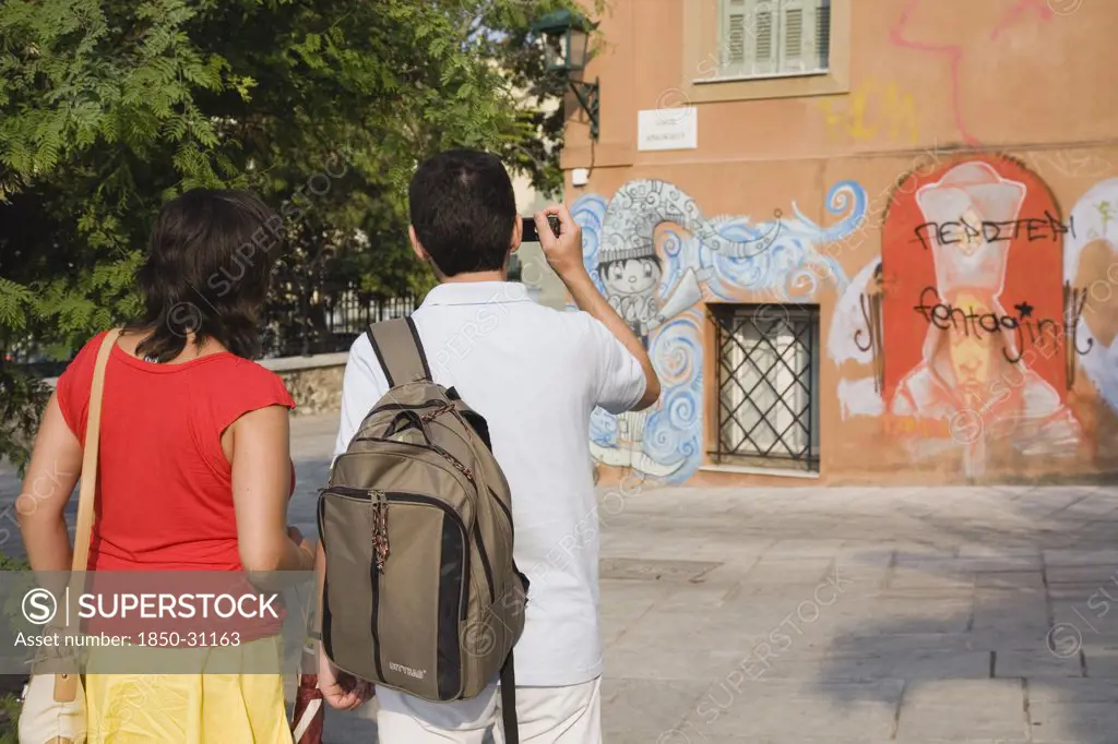 Greece Attica Athens, Tourist couple photographing graffiti on building in Plaka district