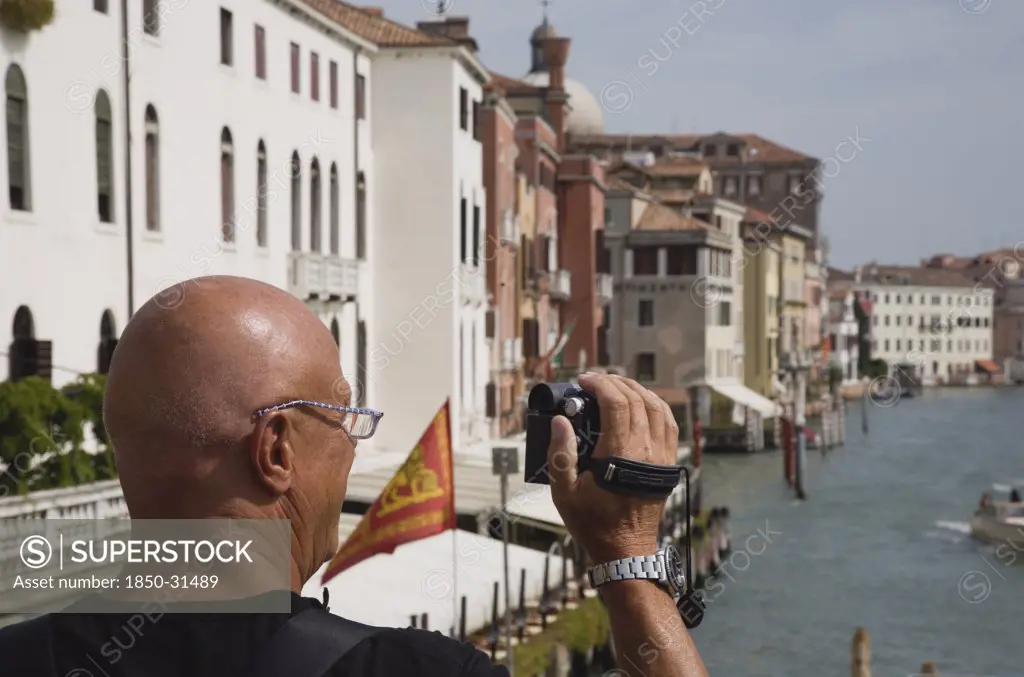 Italy Veneto Venice, Male tourist making a video recording from bridge looking along canal