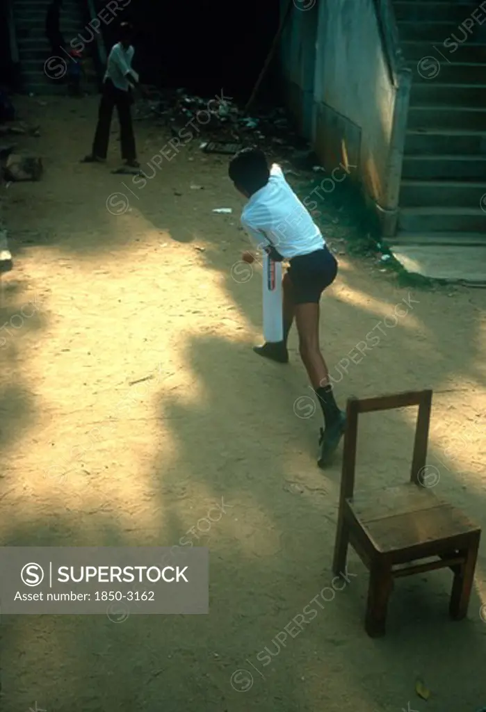 Sri Lanka, Kandy, Young Boys Playing Cricket In Street Using A Wooden Chair As Stumps