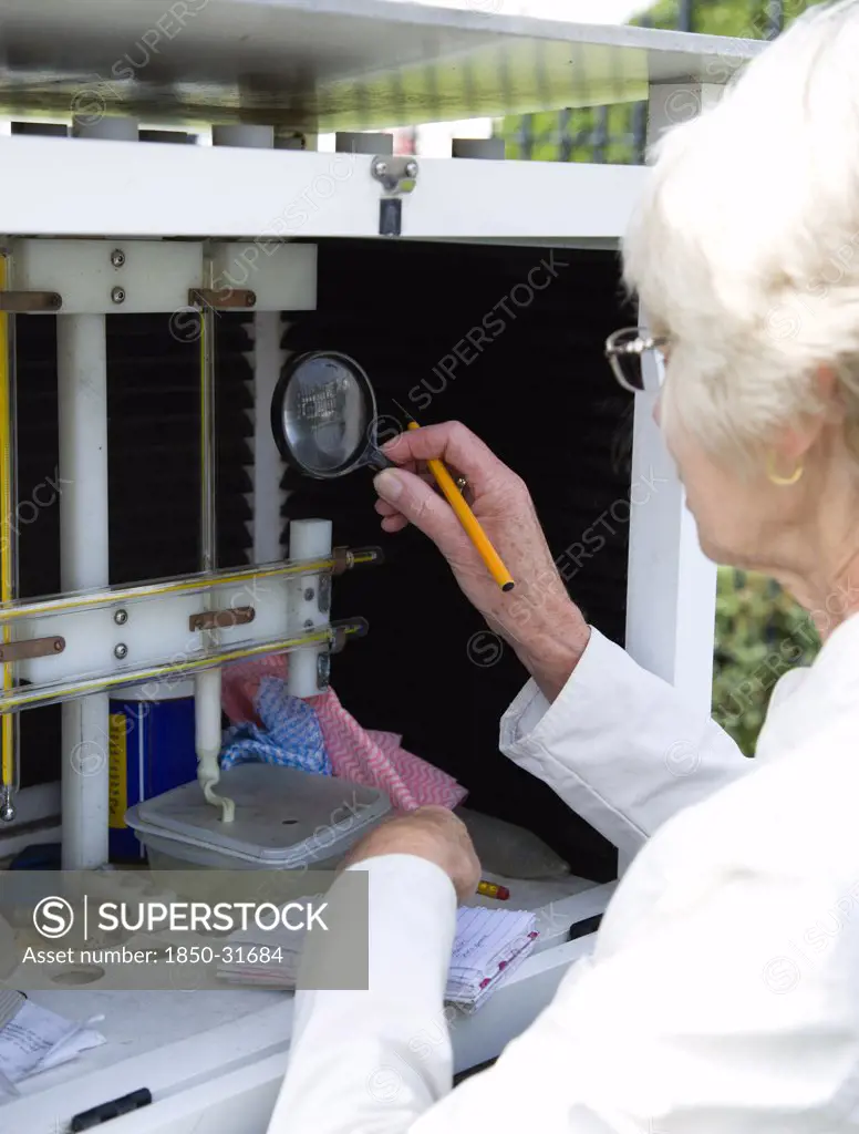Climate, Weather, Measurements, Female weather observer using a magnifying glass to take readings from the wet-bulb thermometer or hygrometer which measures relative humidity in the Stevensons Screen cabinet at Bognor Regis weather station.