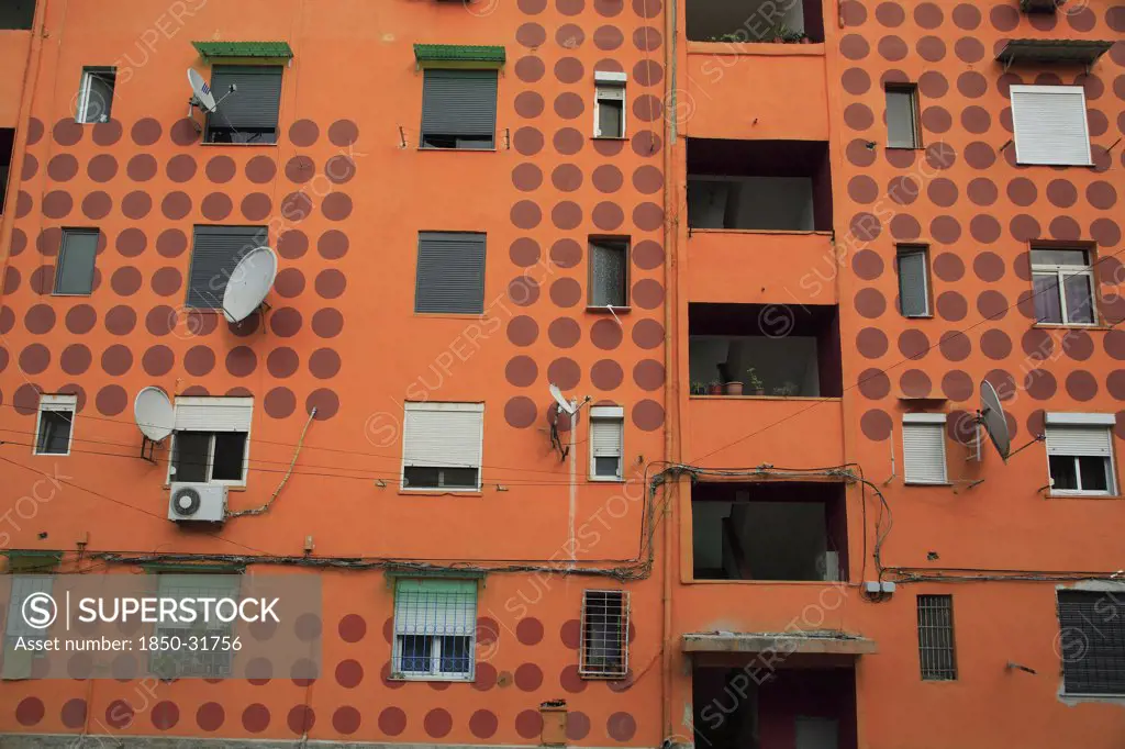 Albania, Tirane, Tirana, Part view of exterior facade of apartment block painted orange with pattern of red painted circles. Multiple windows  satelite dishes  balconies.