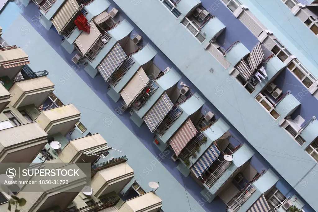 Albania, Tirane, Tirana, Angled view of balconies  striped awnings and satellite dishes on blue painted exterior facade of apartment block.