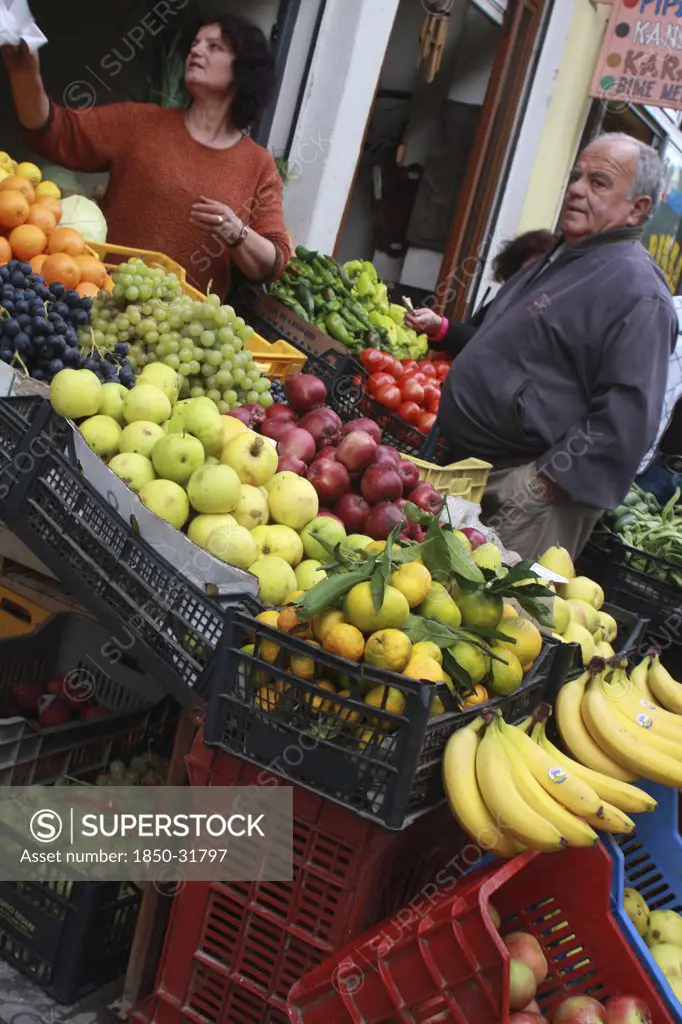 Albania, Berat, Vendor and customer beside display of fruit outside grocers shop.