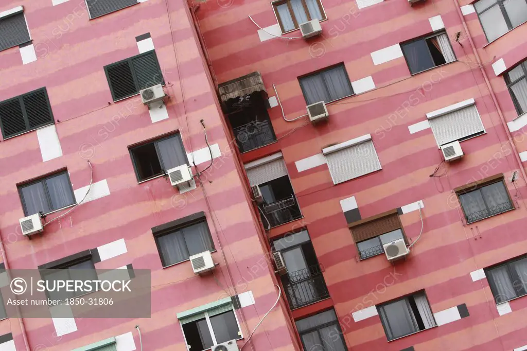 Albania, Tirane, Tirana, Angled part view of pink striped exterior facade of apartment building with air conditioning units.