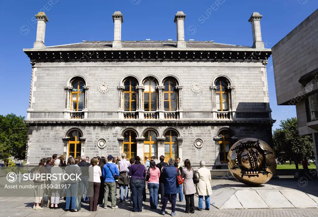 Ireland, County Dublin, Dublin City, Trinity College university Venetian Byzantine inspired Museum Building housing the Geology Department designed by Thomas Deane and Benjamin Woodward and built in 1853-57 and the sculpture Sphere Within Sphere by Arnaldo Pomodoro and a group of sightseeing tourists.
