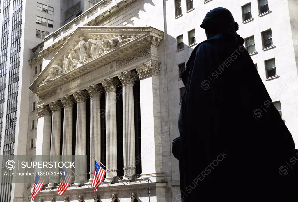 USA, New York, New York City, Manhattan  The New York Stock Exchange building in Broad Street beside Wall Street showing the main facade of the building featuring marble sculpture by John Quincy Adams Ward in the pediment called Integrity Protecting the Works of Man above six tall Corinthian columns with statue of George Washington in the foreground and American Stars and Stripes flags flying from the balcony.
