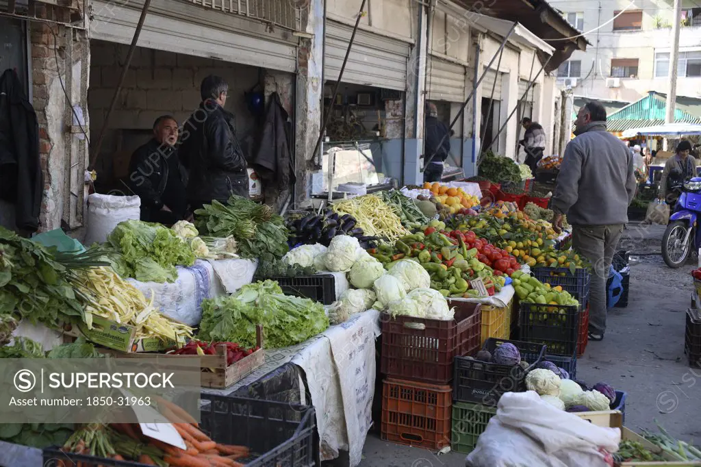 Albania, Tirane, Tirana, Customer and vendors at fruit and vegetable stalls in the Avni Rustemi market with display including carrots  lettuce  aubergines  peppers and oranges.