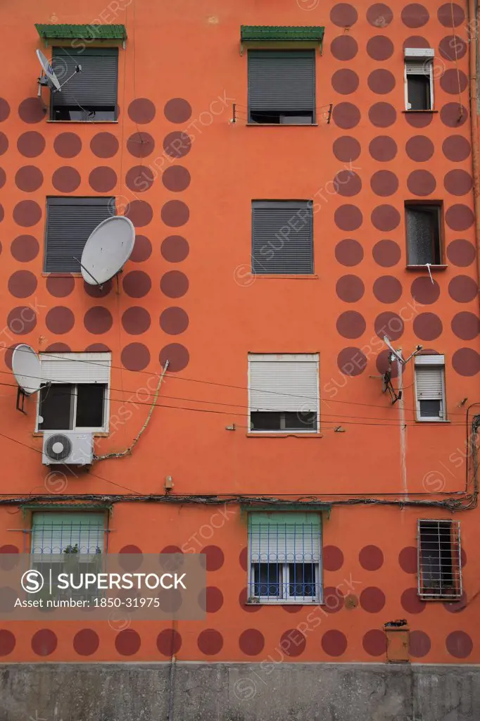 Albania, Tirane, Tirana, Detail of exterior facade of apartment block painted orange with pattern of red circles  multiple windows and satelite dishes.