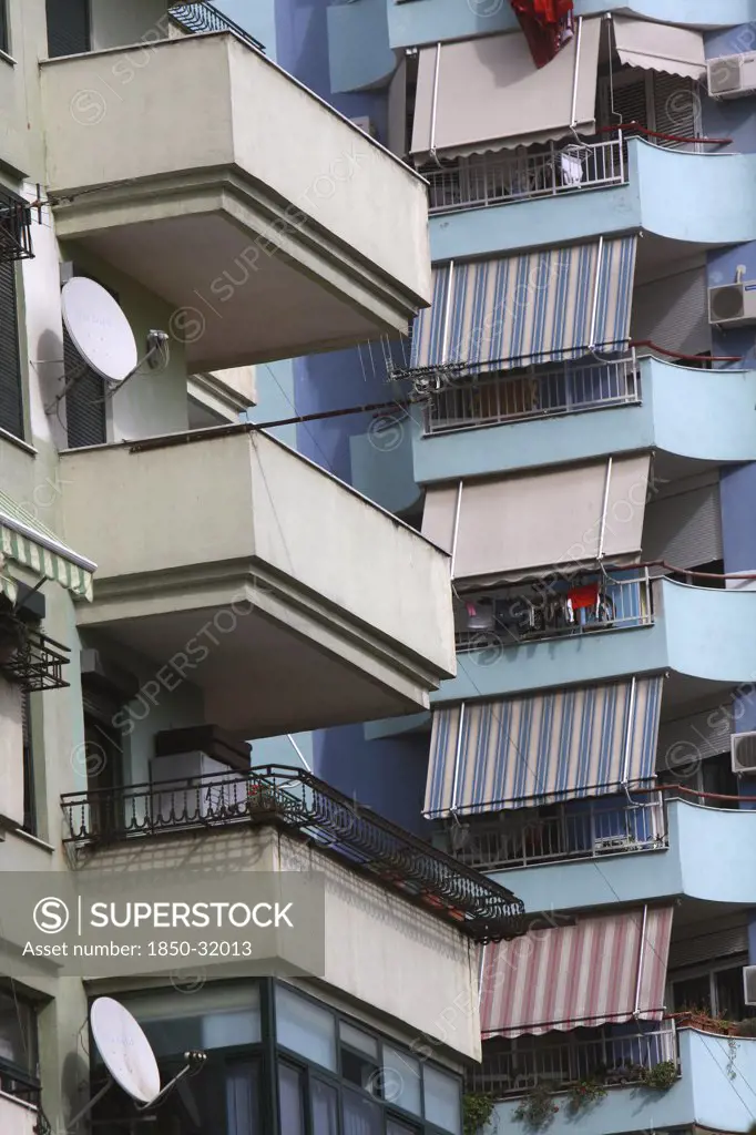 Albania, Tirane, Tirana, Detail of balconies  striped awnings and satellite dishes on blue painted exterior facade of apartment block.