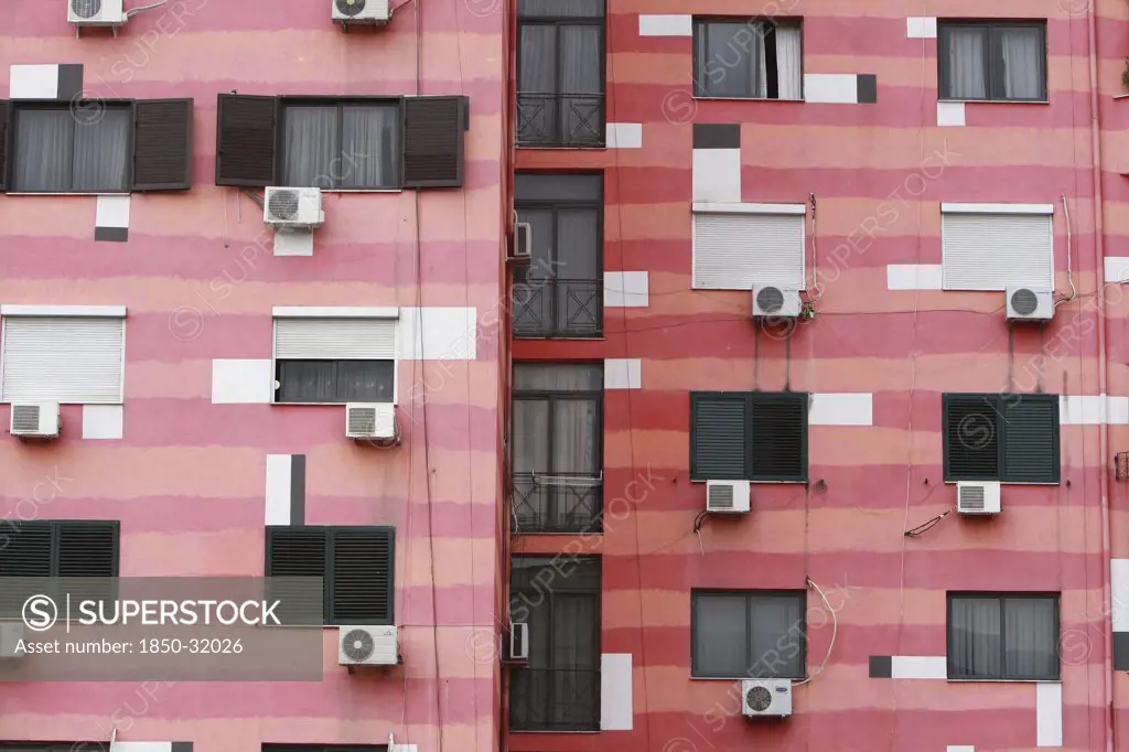Albania, Tirane, Tirana, Part view of pink striped exterior facade of apartment building with air conditioning units.