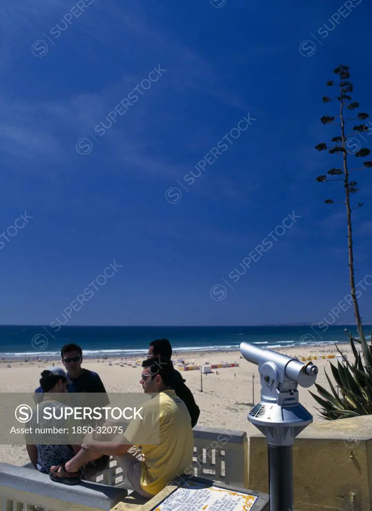 Portugal, Algarve, Praia da Rocha, View along beach with telescope and four young men in foreground