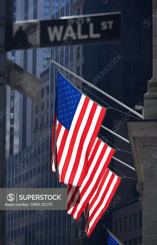 USA, New York, New York City, Manhattan  Road signs for Wall Street and Broad Street with American Stars and Stripes flags flying from the Stock Exchange building.