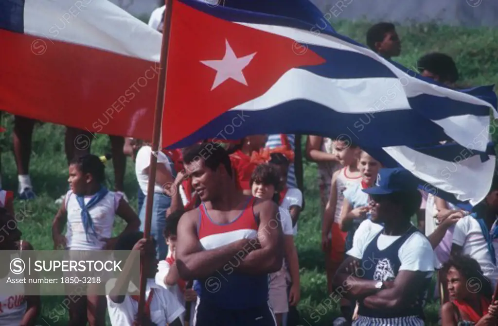 Cuba, Politics, Men Wearing Sports Clothes Standing By Flag Held By One Of A Crowd Of Children Behind