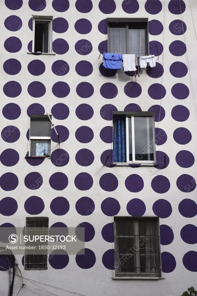Albania, Tirane, Tirana, Part view of exterior facade of apartment block painted with pattern of purple coloured circles. Windows with washing hanging from uppermost.