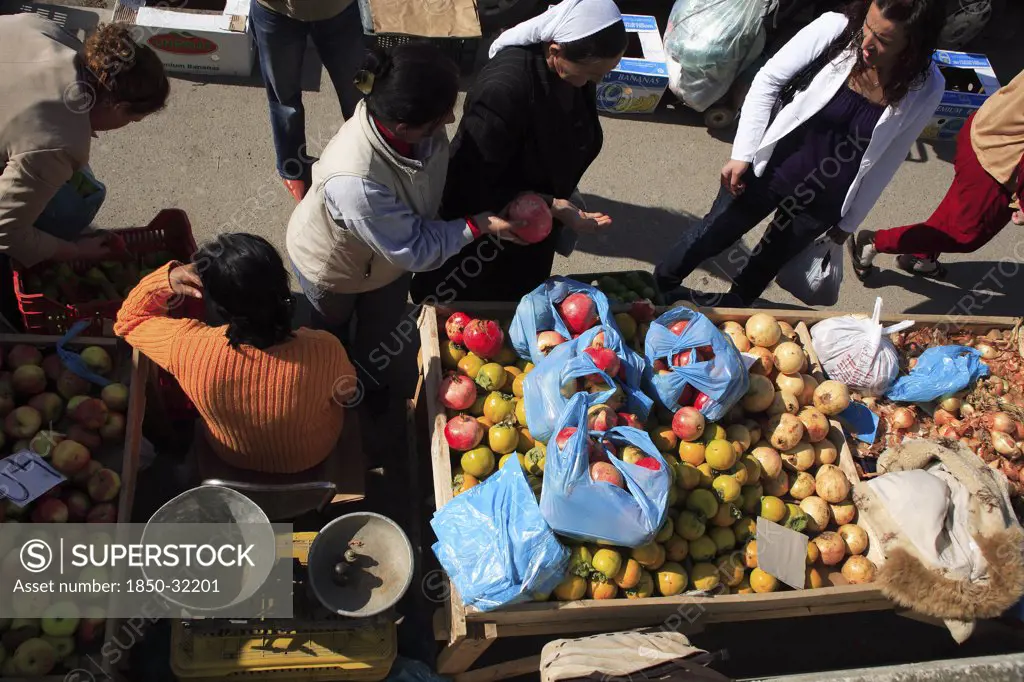 Albania, Tirane, Tirana, Looking down on stall of street vendor selling apples  pomegranates and onions sitting beside set of scales with female customers making purchases.