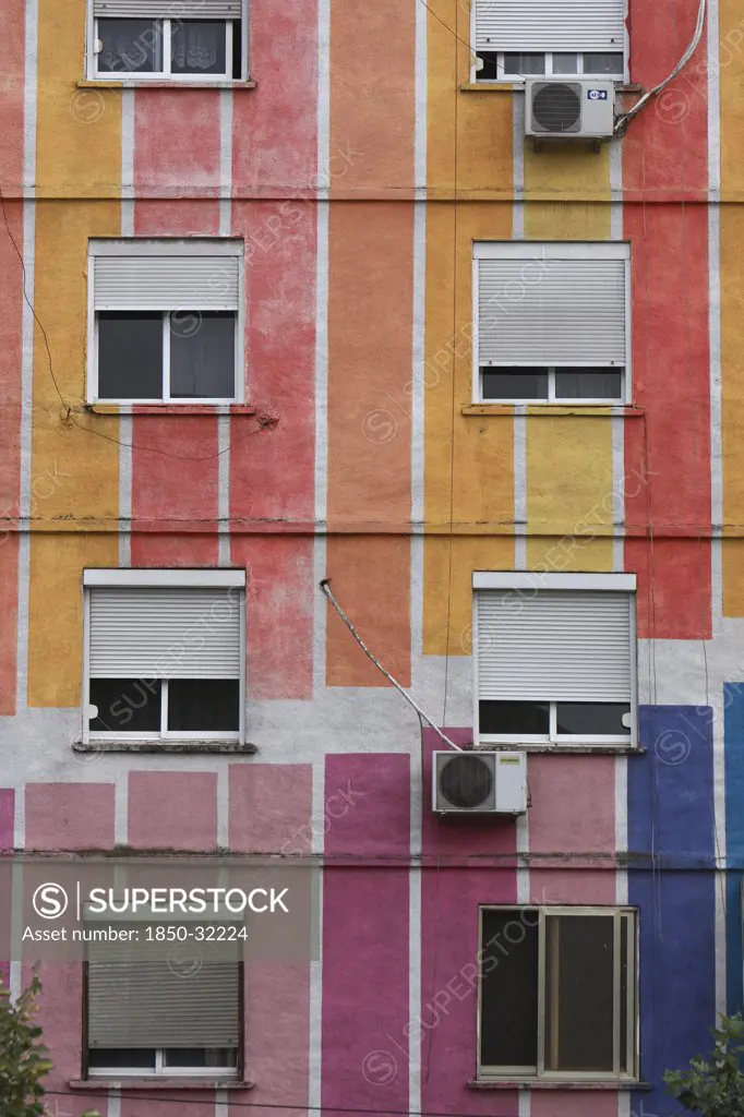 Albania, Tirane, Tirana, Detail of exterior facade of striped  multi-coloured apartment block with windows  window blinds and air conditioning units.