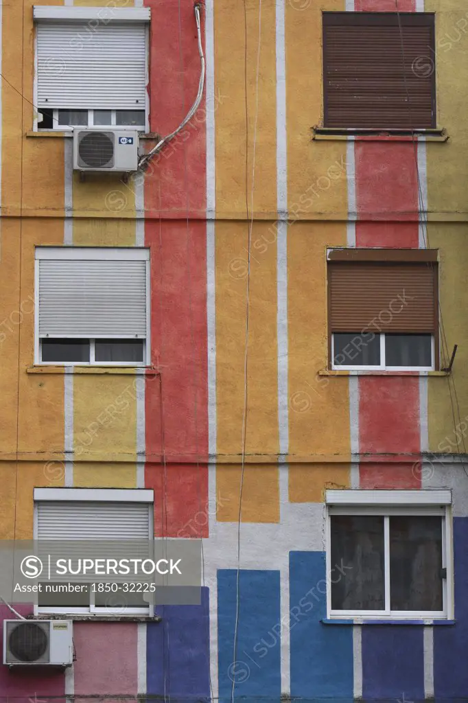 Albania, Tirane, Tirana, Detail of exterior facade of striped  multi-coloured apartment block with windows  window blinds and air conditioning units.