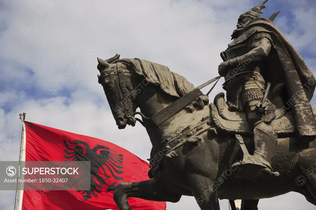 Albania, Tirane, Tirana, Skanderbeg Square. Part view of equestrian statue of national hero George Castriot Skanderbeg also known as The Dragon of Albania beside red flag with double headed eagle emblem.