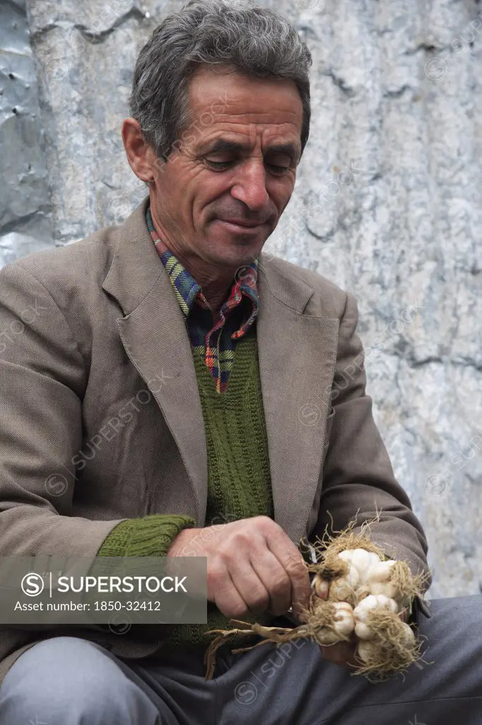 Albania, Tirane, Tirana, Portrait of a male street vendor bunching bulbs of garlic together for sale.