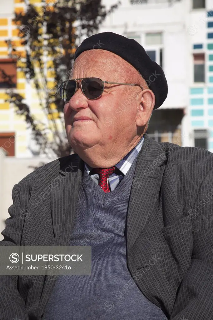 Albania, Tirane, Tirana, Head and shoulders portrait of an elderly man wearing beret and sunglasses. Three-quarter profile left.