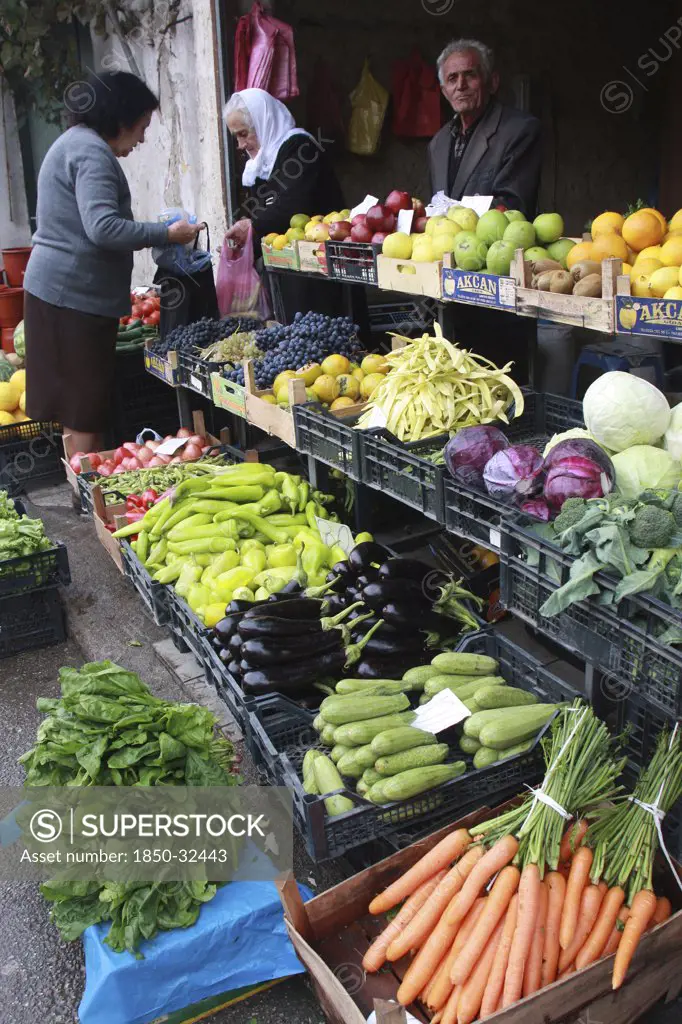 Albania, Tirane, Tirana, Customers and vendor beside display of fruit and vegetables at grocers in the Avni Rustemi market.