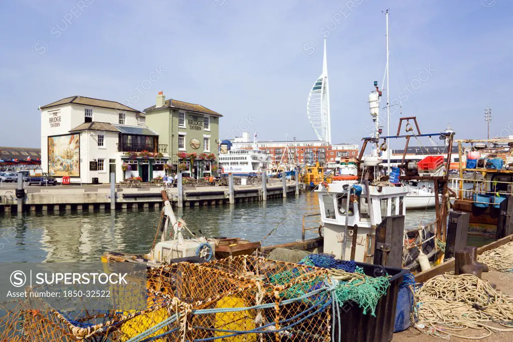 England, Hampshire, Portsmouth, The Camber in Old Portsmouth showing the Spinnaker Tower beyond the Bridge Tavern with a mural by Thomas Rowlanson of his cartoon entitled Portsmouth Point with fishing boats moored at the quayside.