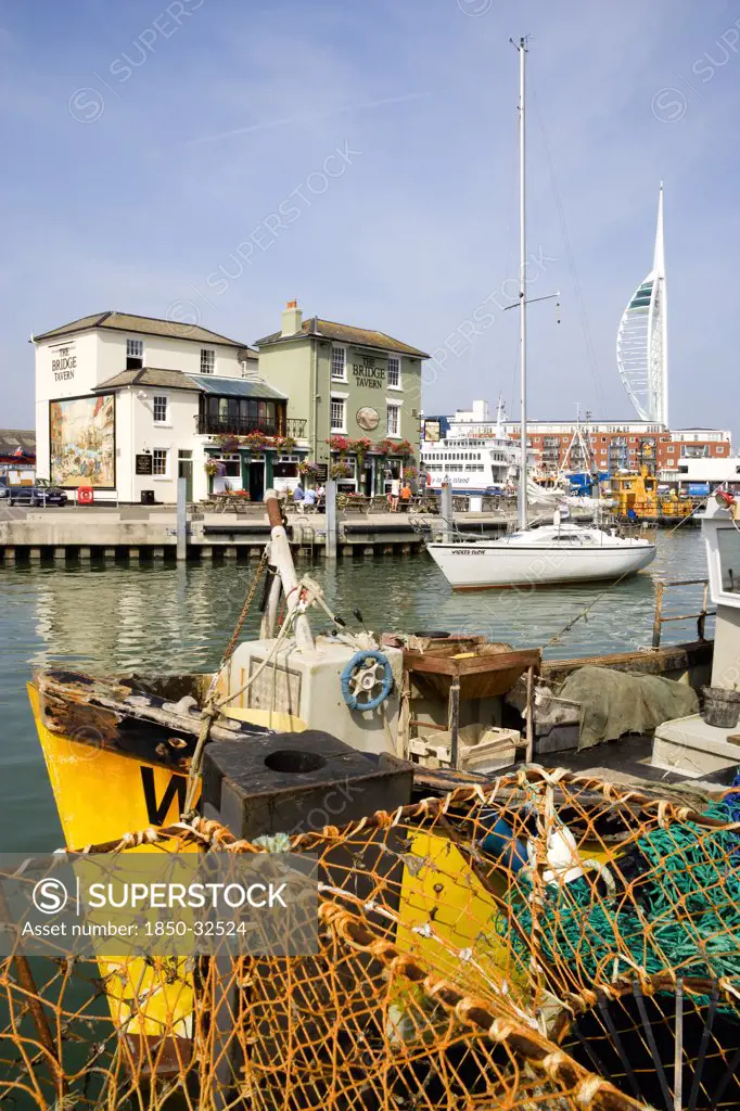 England, Hampshire, Portsmouth, The Camber in Old Portsmouth showing the Spinnaker Tower beyond the Bridge Tavern with a mural by Thomas Rowlanson of his cartoon entitled Portsmouth Point with fishing boats moored at the quayside and sailing yacht entering harbour.