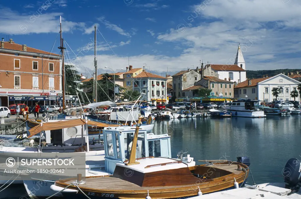 Slovenia, Koper, Port with fishing boats moored and cars parked on the quayside.