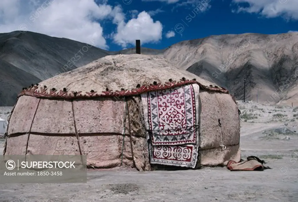 China, Xinjiang, Karakol Lake Area, Khirgiz Yurt In Barren Mountain Landscape With Decorated Textile Hanging Over Door