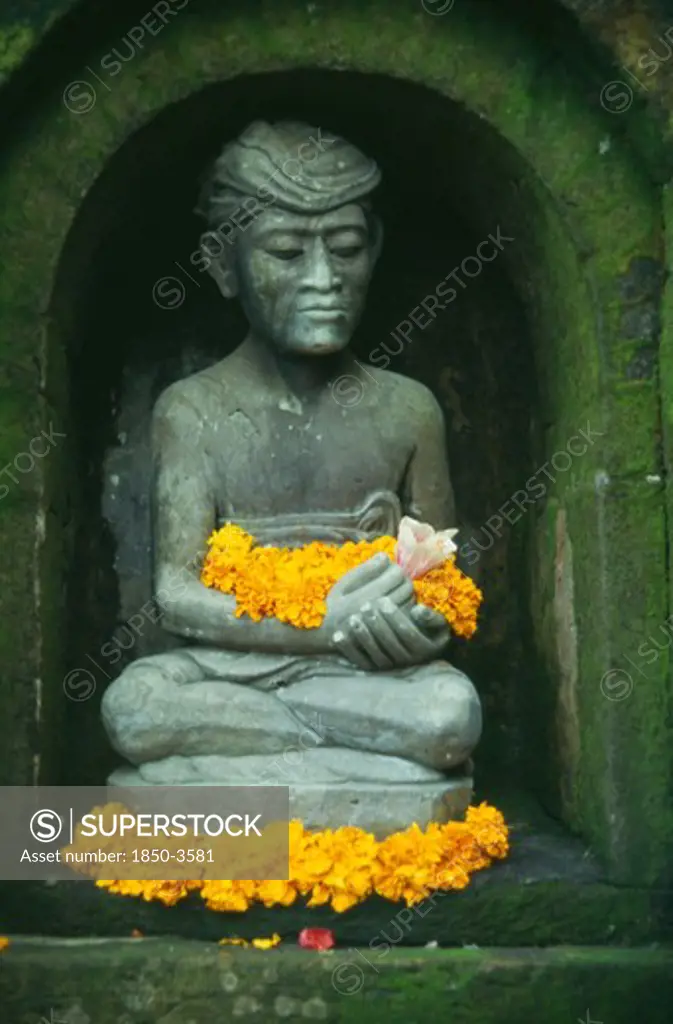 Indonesia, Bali, Ubud, Small Hindu Shrine Detail Of Seated Figure With Flower Offerings In The Miro Garden Restaurant