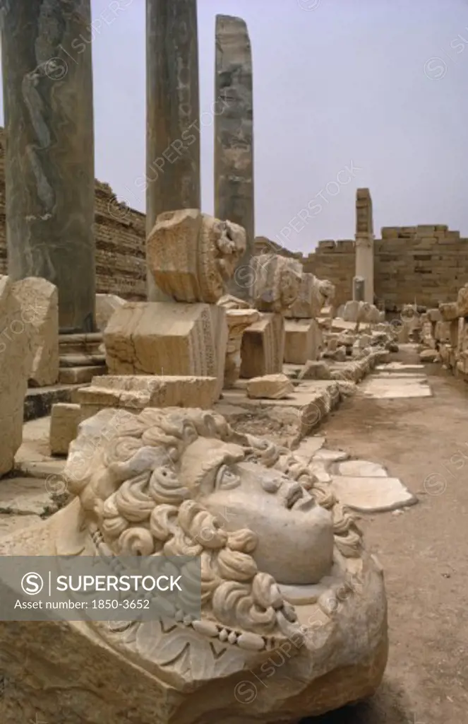 Libya , Leptis Magna, Roman Ruins Of The New Forum With Carved Face In The Foreground And Green Marble Pillars Behind