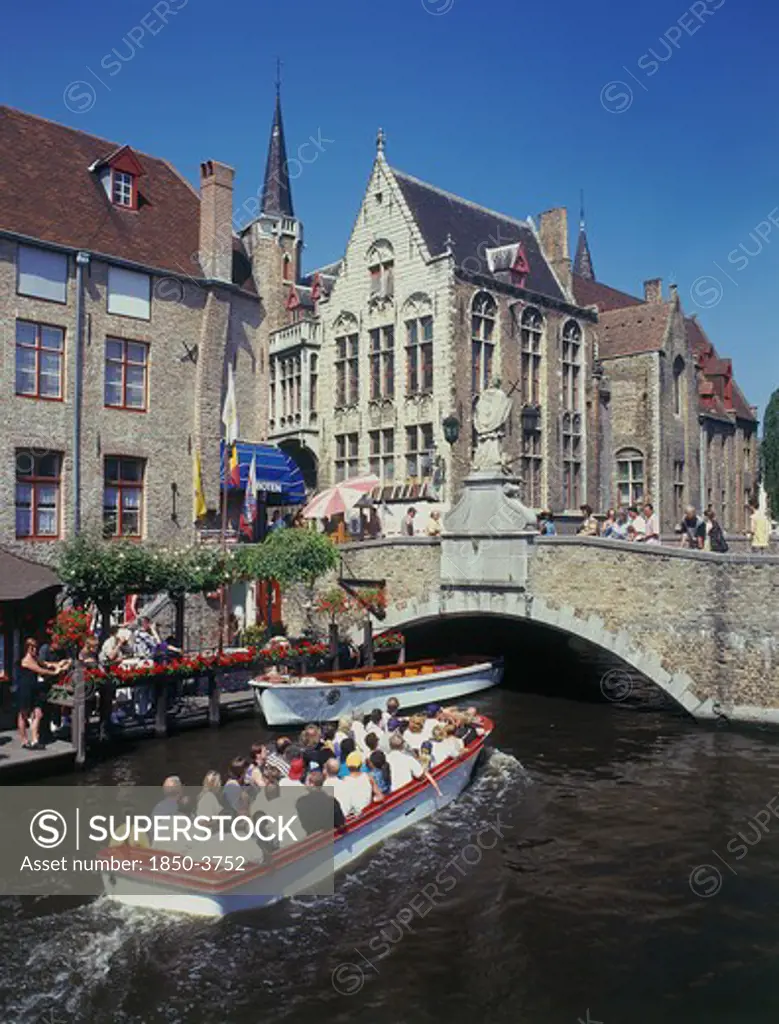 Belgium, West Flanders, Bruges, Tourists On Boat Trips On A Canal With Old Bridge And Houses Behind