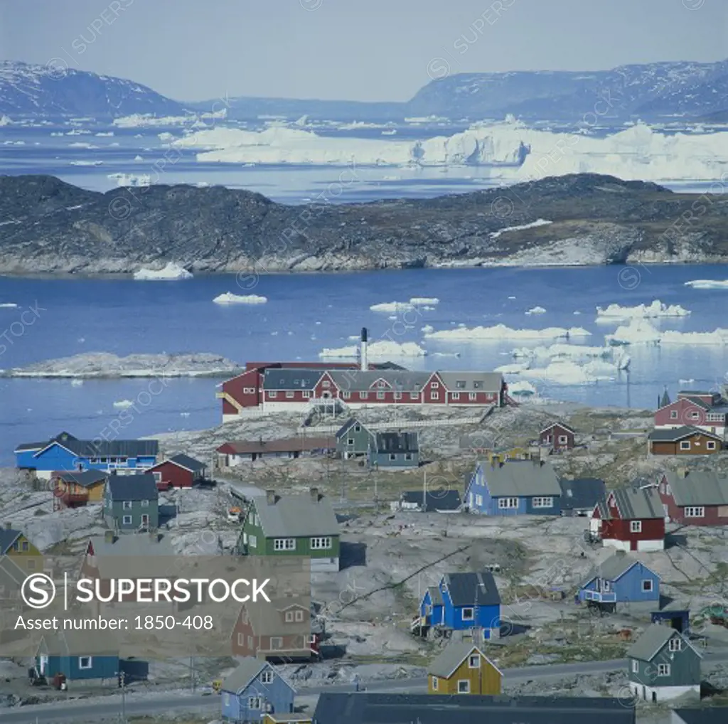 Greenland, Denmark, Jakobshaven, View Over Ilulissat Town With The Sea And Icebergs Beyond Coloured Houses On Rock