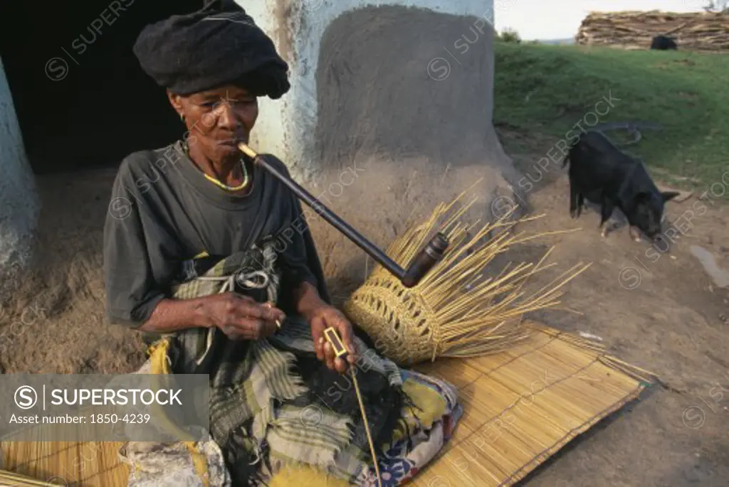 South Africa, Eastern Cape, Coffee Bay, Elderly Xhosa Woman Making Basket And Smoking Long Pipe.
