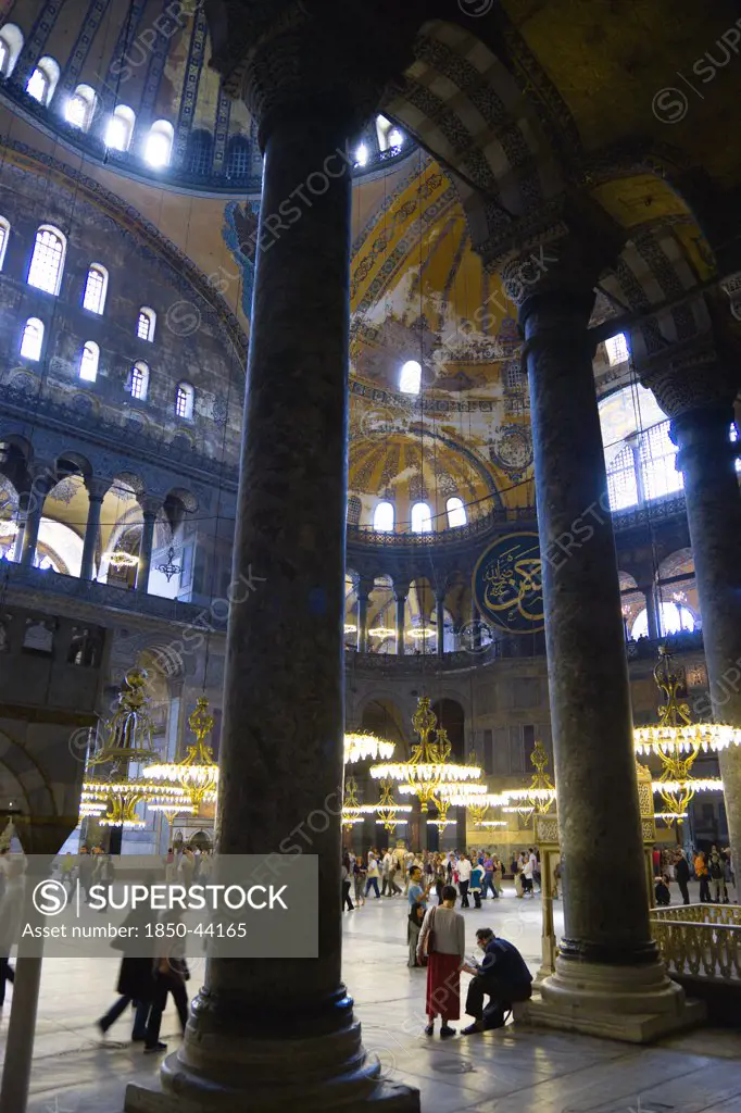 Turkey,  Istanbul, Sultanahmet Haghia Sophia Sightseeing tourists beneath the dome with murals and chandeliers in the Nave of the Cathedral.