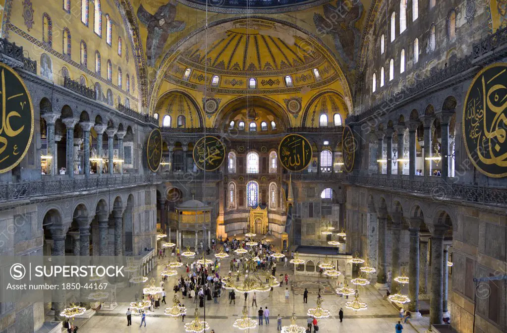 Turkey,  Istanbul, Sultanahmet Haghia Sophia Sighseeing tourists beneath the dome with murals and chandeliers in the Nave of the Cathedral.