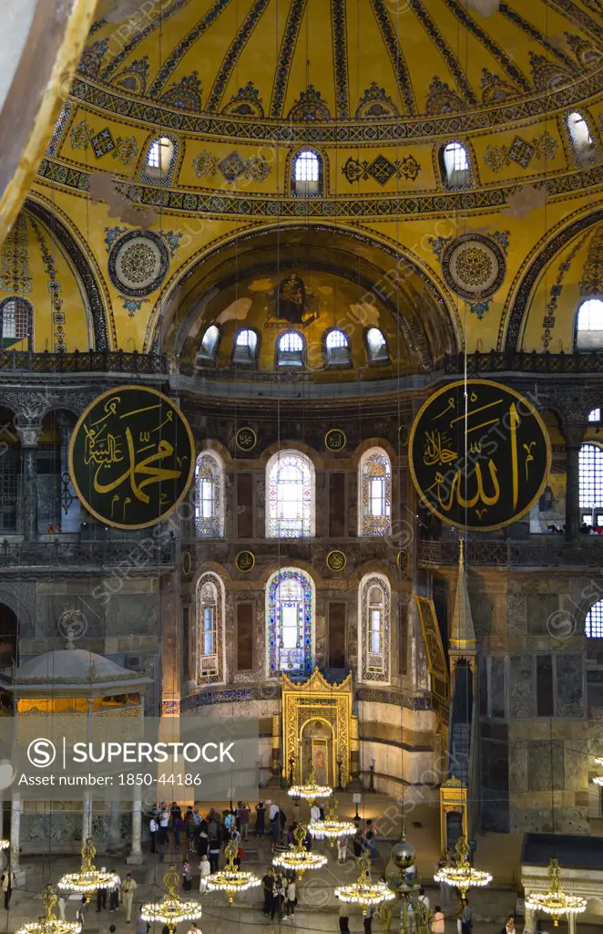 Turkey,  Istanbul, Sultanahmet Haghia Sophia Sightseeing tourists beneath the dome with murals and chandeliers in the Nave of the Cathedral with calligraphic roundels of Arabic Koran texts above the Lodge of The Sultan.
