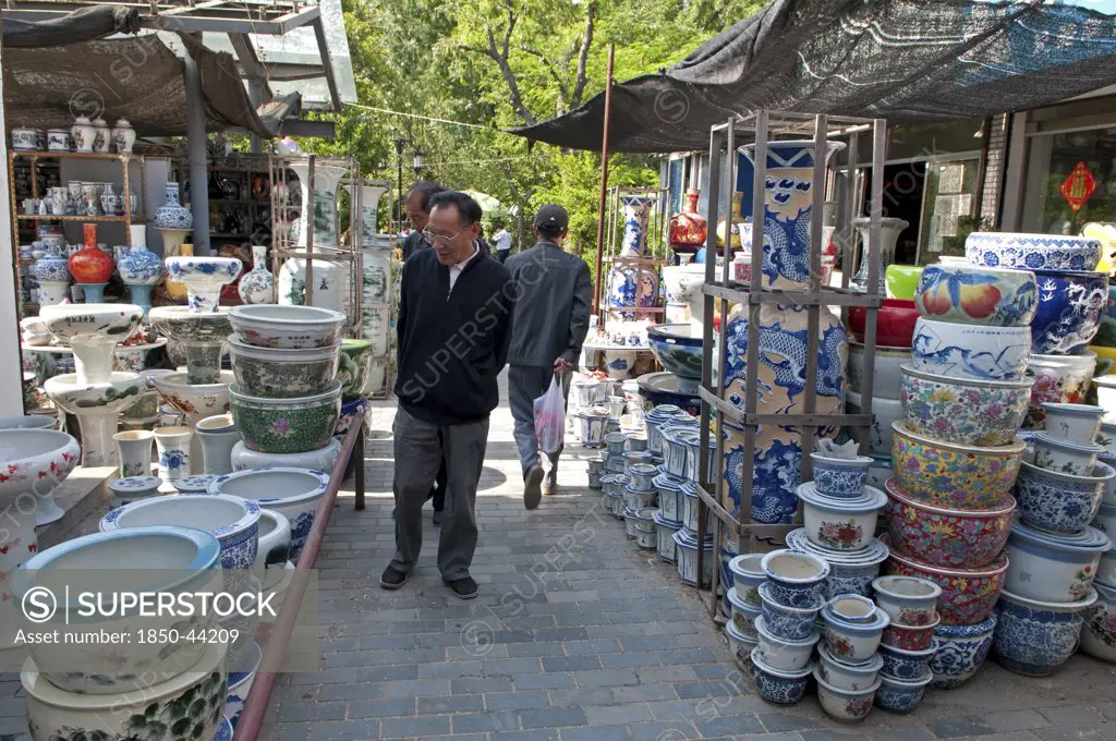 China, Jiangsu, Yangzhou, Ceramic pots for plants and decorative use in downtown canal-side street market. Man strolling through market looking at pots. Trees in background. Marco Polo once served as a municipal official of the city. Trevor Page