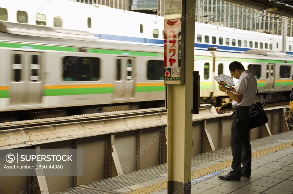 Japan, Honshu, Tokyo, Commuter on platform cooling himself with paper fan whilst waiting for his train