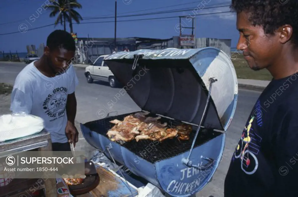 West Indies, Jamaica, Market, Man Cooking Jerk Chicken On Roadside Stall With Waiting Customer.