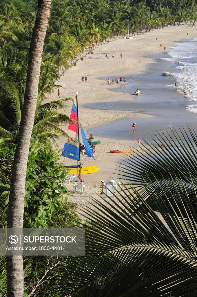 View onto Playa la Ropa with a colourful sailboat on sandy beach lined with palm trees.Mexico Guerrero Zihuatanejo