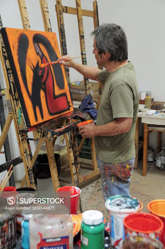 Artist Juan Ezcurdia in his studio working on painting set on easel.Mexico Bajio San Miguel De Allende