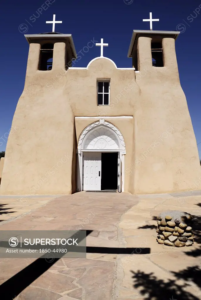 Church of San Francisco de Asis. Exterior of church with deep shadow of cross cast across path to entrance in foreground.USA New Mexico Taos