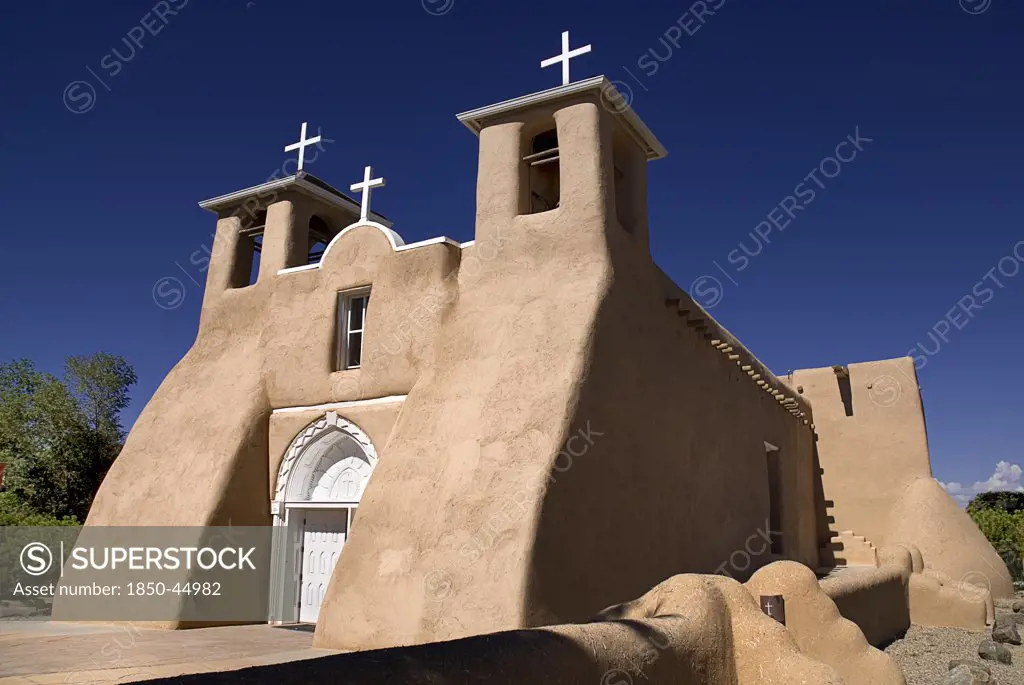 Church of San Francisco de Asis. Angled view of adobe style exterior facade with white painted crosses on rooftop and bell towers.USA New Mexico Taos