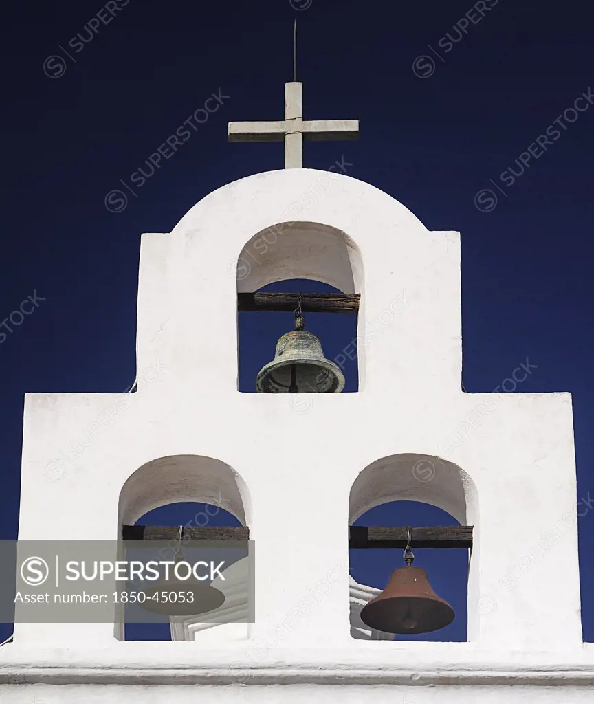 Mission Church of San Xavier del Bac. White painted bell tower with three bells and topped with a cross.USA Arizona Tucson